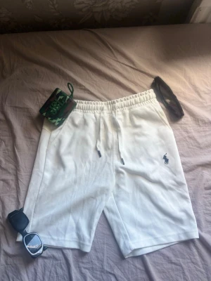 Vita shorts med snörning från Polo Ralph Lauren - Säljer ett par vita shorts från Polo Ralph Lauren med klassisk broderad logga på benet. Shortsen har elastisk midja med snörning och är tillverkade i mjuk bomull, perfekta för sommardagar. Enkel och clean design som passar till det mesta.Pris kan diskuteras.