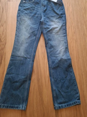 Blå bootcut jeans med slitningar - Ett par klassiska blå bootcut jeans med lätt slitna detaljer framtill och baktill. Jeansen har fem fickor och normal midja. Materialet är denim i bomull och passformen är något utsvängd nedtill för en retro vibe.