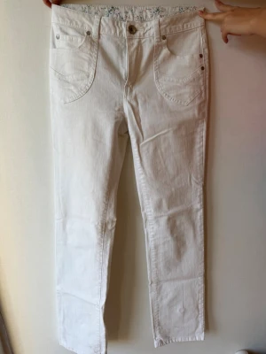 Vita jeans från Flash, storlek 36 - Snygga vita jeans från Flash i storlek 36. Modellen har raka ben, fem fickor och silverfärgade nitar. Materialet är en mix av bomull, polyester och elastan för skön stretch. Insidan av linningen har ett gulligt blommigt mönster.