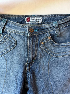 Blå bootcut jeans med detaljer - Snygga blå bootcut jeans från Newstone style med unika sömmar och dekorativa fickor framtill. Jeansen har klassisk knappgylf och bälteshällor. Materialet är denim i bomull och passformen är något utsvängd nedtill.
