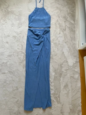 Blått ribbat set med kjol och topp L  - Säljer ett snyggt blått set med ribbad struktur. Setet består av en crop top med tunna axelband och en lång omlottkjol med knytning i midjan. Materialet är stretchigt och mjukt, perfekt för en trendig look.
