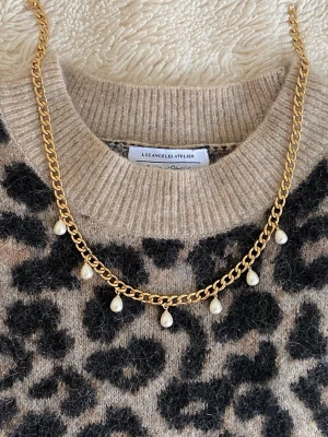 Guldhalsband med droppformade pärlor - Snyggt halsband i guldfärgad rostfritt med sju droppformade pärlor som hänger längs kedjan. Kedjan har en klassisk, lite chunky design och pärlorna ger en elegant touch. Perfekt för att lyfta vilken outfit som helst med en trendig och stilren vibe.