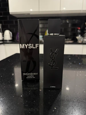 YSL MYSLF Le Parfum - En stilren parfymflaska i matt svart med YSL-logga i relief. Flaskan är rektangulär med svart lock och kommer i en matchande svart kartong med tydlig MYSLF-etikett. Perfekt för dig som gillar exklusiva dofter och snygg design.