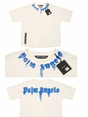 Vit Palm Angels t-shirt med blå text - Säljer en vit t-shirt från Palm Angels med blå graffiti-inspirerad text runt halsen och på ryggen. T-shirten har normal passform och är kortärmad. Tillverkad i mjuk bomull, perfekt för en streetwear-look.