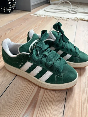 Gröna Adidas Campus sneakers - Säljer ett par gröna Adidas Campus sneakers i mocka med klassiska vita ränder på sidorna och vit sula. Skorna har gröna skosnören och vit insida. Köpta på Zalando. Kvitto finns. 