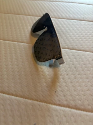 Svarta solglasögon med monogram - Snygga svarta solglasögon med rektangulär sköldformad lins och diskret monogrammönster över hela glaset. Glasögonen har en modern och edgy look med mörka linser och silverfärgade detaljer. Perfekta för dig som vill sticka ut med en unik accessoar.