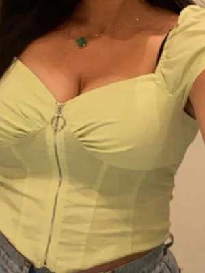 Ljusgul croppad topp med dragkedja - Trendig ljusgul croppad topp med korta puffärmar och markerad byst. Toppen har en snygg dragkedja framtill med ringdetalj och är figurnära i modellen. Perfekt att styla med höga jeans för en cool look.