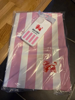 Rosa Moln mobilskal med ränder - Merch Snyggt mobilskal i vitt och rosa med Rosa Mjölk-loggan och text. Skalets design har rosa ränder och en tecknad figur. Passar dig som vill ha ett unikt och lekfullt mobilskal. Materialet är hårdplast.