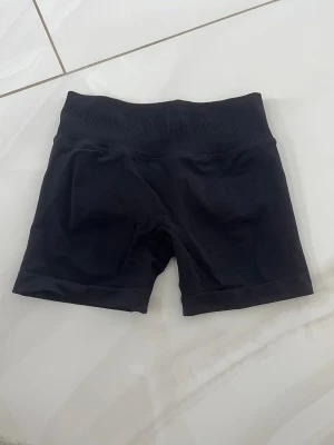 Svarta tighta cykelshorts - Svarta cykelshorts med bred ribbad midja och tight passform. Perfekta för träning eller som basplagg till vardags. Tillverkade i stretchigt syntetmaterial för maximal komfort och rörelsefrihet.