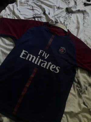 PSG Neymar Jr matchtröja blå/röd - Säljer en officiell Paris Saint-Germain matchtröja i blått och vinrött med Neymar Jr och nummer 10 på ryggen. Tröjan har Fly Emirates-tryck på bröstet och PSG-logga. Perfekt för dig som älskar fotboll och vill stötta ditt favoritlag.