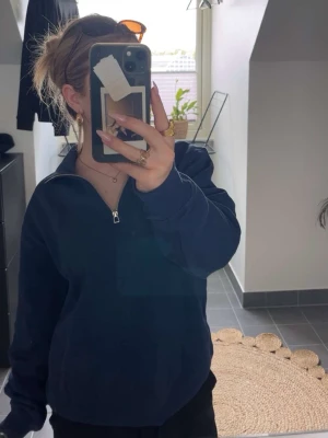 Mörkblå halfzip hoodie - En enkel och stilren mörkblå hoodie med halv dragkedja framtill. Hoodien har en hög krage och är gjord i ett mjukt material som känns skönt mot huden. Perfekt för dig som gillar en avslappnad och clean look. Långa ärmar och rymlig passform.