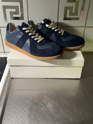 Mörkblå maison margiella sneakers - Snygga mörkblå sneakers med kontrasterande partier i mocka och slätare material. Skorna har vita snören och en klassisk gummisula i beige. Perfekt för dig som gillar stilrena och tidlösa sneakers med en modern twist.