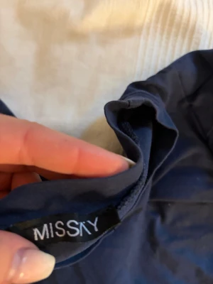 Mörkblå topp med volang från Missky - Snygg mörkblå topp från Missky med korta ärmar och volangdetalj längs axeln. Perfekt för dig som vill ha något enkelt men ändå med en twist. Mjuk och skön känsla, passar till många olika outfits.