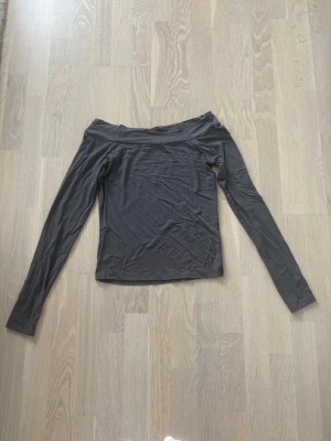 Grå offshoulder långärmad topp - Snygg grå offshoulder topp med långa ärmar och figurnära passform. Tillverkad i ett stretchigt och mjukt material som sitter skönt på kroppen. Perfekt att styla med jeans eller kjol för en trendig look. En riktig favorit från min sida! Passar de som bär Small även!