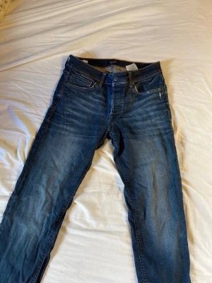 Jack and Jones jeans  - Snygga mörkblå jeans med klassisk femficksdesign och raka ben. Jeansen har subtila slitningar framtill och är tillverkade i denim. Perfekta för en avslappnad och trendig look.