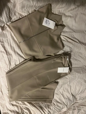 Beige tracksuit från Les Deux - Snyggt beige tracksuit-set från Les Deux med dragkedja på jackan och matchande byxor med dragsko i midjan. Kvitto medföljer 