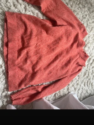 Korallröd stickad tröja - Mysig stickad tröja i en snygg korallröd färg. Tröjan har rund halsringning, långa ärmar och ribbade muddar vid ärmslut och nederkant. Materialet ser ut att vara mjukt och fluffigt!!