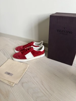 Röda sneakers från Valentino Garavani - Snygga röda sneakers från Valentino Garavani i mocka med vita detaljer och vit sula. Klassisk låg modell med svart snörning och stilren design. 