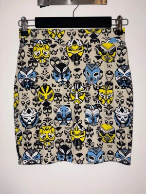 Mönstrad kortkjol från Monki - Säljer en beige kortkjol från Monki med färgglatt maskmönster i svart, blått och gult. Kjolen är i mjuk bomull med lite stretch för skön passform. Perfekt för dig som vill sticka ut med en unik och lekfull stil.