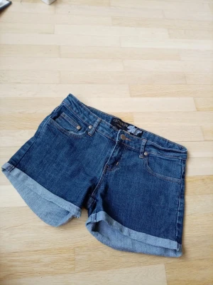 Blå jeansshorts från Cotton On - Snygga blå jeansshorts från Cotton On med uppvikta benslut och klassisk femficksdesign. Shortsen har normal passform och är tillverkade i slitstarkt denimtyg, perfekta för varma dagar.