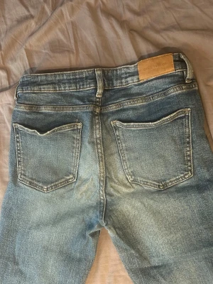 Blå bootcut jeans från Gina Tricot - Säljer ett par blå bootcut jeans från Gina Tricot utan mönster på fickorna. Byxorna har låg midja och reglerbar resår i midjan. 
