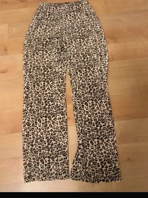 Leopardmönstrade mjukisbyxor Gina Tricot - Säljer ett par leopardmönstrade mjukisbyxor från Gina Tricot i storlek XS. Byxorna har rak passform, resår i midjan och är gjorda i mjukt material med 95% polyester och 5% elastan. Perfekta för en chill och trendig look.