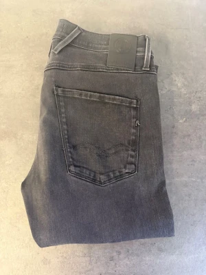 Svarta slim fit jeans från Replay 31/32 - Säljer ett par svarta slim fit jeans från Replay med klassisk femficksdesign och diskret logga på bakfickan. Jeansen har normal midja och raka ben i mjuk bomullsdenim. Perfekta för en clean och stilren look.
