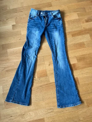 Blå bootcut jeans med utsvängda ben - Säljer ett par klassiska blå bootcut jeans med utsvängda ben och fem fickor. Jeansen har normal midja och är gjorda i denim med lätt tvättad look. Perfekta för dig som gillar retrostil och vill ha ett par bekväma jeans med snygg passform.