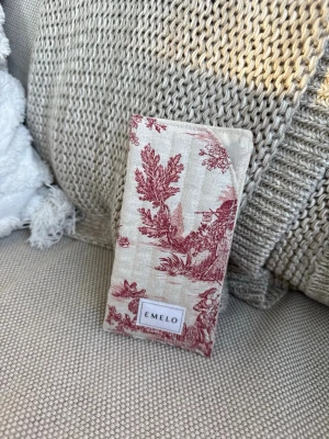 Mönstrat glasögonfodral från Emelo - Snyggt fodral i beige tyg med vinrött franskt mönster från Emelo. Perfekt för att förvara dina glasögon. Tygmaterialet ger en mjuk känsla och den stilrena designen gör det till en cool accessoar.