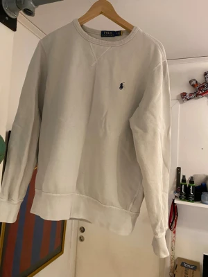 Beige sweatshirt från Polo Ralph Lauren - Snygg beige sweatshirt från Polo Ralph Lauren med klassisk rund halsringning och broderad logga på bröstet. Tröjan har ribbade muddar och är tillverkad i mjukt bomullsmaterial. Perfekt för en avslappnad och stilren look. Är urtvättad därav billigt pris