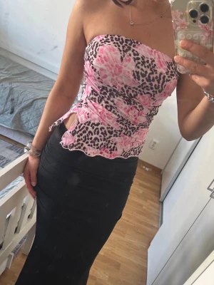 Rosa leopard bandeau tubtopp - Snygg bandeau tubtopp med rosa blommor och leopardmönster. Toppen är ärmlös och har vågig kant nertill samt en liten slits på sidan. Perfekt för dig som vill sticka ut med ett unikt mönster och cool vibe.