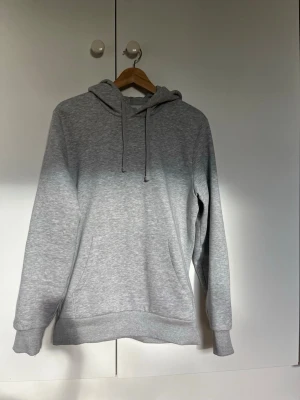 Grå basic hoodie med huva - En stilren grå hoodie med huva och dragsnören. Klassisk känguruficka framtill och ribbade muddar vid ärmar och nederkant. Perfekt för en avslappnad och enkel look. Tillverkad i mjukt sweatshirtmaterial. Knappt använd