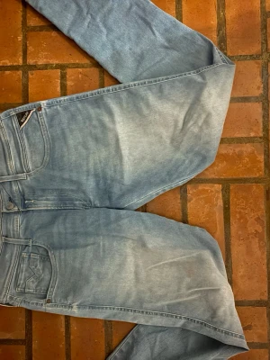 Ljusblå raka jeans från Replay - Säljer ett par ljusblå jeans från Replay med klassisk femficksmodell och raka ben. Jeansen har en snygg tvättad look och detaljer som Replay-lapp bak i midjan. Perfekta för en avslappnad och trendig stil.