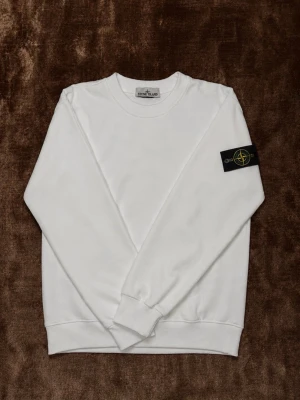 Vit sweatshirt från Stone Island S - Säljer en clean vit sweatshirt från Stone Island med klassisk rund hals och ribbade muddar. Tröjan har den ikoniska svarta patchen med logga på vänster ärm. Perfekt för dig som gillar stilrena och trendiga plagg.Pris kan diskuteras. 😊