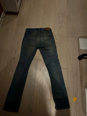 Blå slim fit nudie jeans - Säljer ett par blå slim fit jeans med snygga slitningar och tvättade detaljer. Klassisk femficksmodell med raka ben och normal midja. Jeansen har en läderpatch bak i midjan och är tillverkade i denim, troligtvis bomull. Perfekta för en avslappnad och trendig look. Dom är i storlek 30W L32. Jag är 171 och väger 56kg jag tycker dom sitter bra på mig väldigt snygga. Modell är Grim Tim 