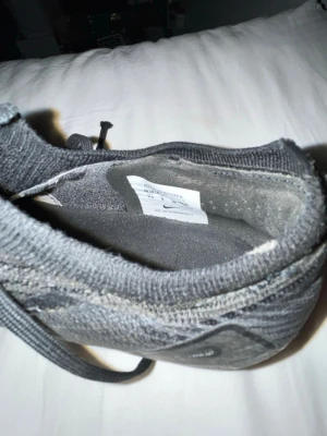 Svarta Nike fotbollskor i textil - Snygga grå sneakers från Nike med ovandel i stickad textil och klassisk snörning. Skon har en låg profil och diskret Nike-logga på sidan. Perfekt för dig som gillar stilrena och bekväma sneakers.