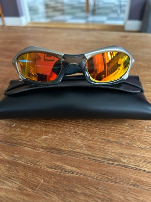 Oakley splice  - Säljer ett par riktigt coola Oakley solglasögon med sportig design. Bågarna är i silverfärgad syntet och glasen har en spegeltonad guldfärg som skiftar i orange. Perfekta för dig som vill sticka ut och gillar futuristisk stil. Svart fodral medföljer.