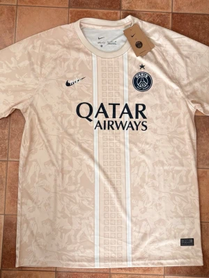 PSG (Helt ny med tags!) – Storlek XL - Säljer en helt ny och oanvänd Paris Saint-Germain. Tröjan har kvar alla originaltags och kommer i sin plastförpackning. Riktigt snygg och stilren design i en exklusiv beige/cream färg med unika detaljer och den klassiska retro Nike-loggan! 