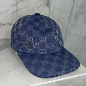 Blå Mönstrad keps  - Säljer en blå kepsi med det klassiska mönstret över hela kepsen. Kepsen har böjd skärm och är tillverkad i ett denimliknande material. Perfekt för dig som vill ha en stilren accessoar med lyxig känsla.