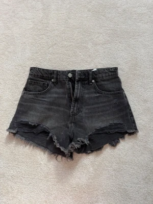 Svarta jeansshorts från Zara - Coola svarta jeansshorts med hög midja och råa, fransiga kanter. De har klassiska fem fickor och slitna detaljer framtill som ger en edgy look. Perfekta för sommarens alla äventyr och passar till sneakers eller boots. Säljer för att jag aldrig använt dem, så de är i helt nytt skick utan lapp. ⭐️🩵