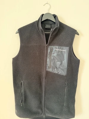 Svart fleeceväst Peak Performance - svart väst från Peak Performance med dragkedja och tre fickor, varav en bröstficka med logotyp. Materialet är mjukt och värmande, perfekt för inför vår/höst väder! Hör av er vid funderingar!