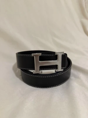 Svart H bälte - Svart H-bälte i fint skick. Stilren modell som passar till allt. Hör av dig gärna vid intresse.