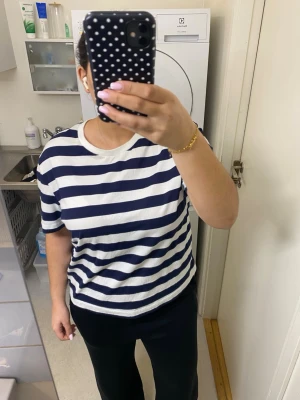 Randig t-shirt i marinblått och vitt - Säljer en klassisk randig t-shirt med breda marinblå och vita ränder. T-shirten har rund halsringning och korta ärmar. Perfekt för en avslappnad och stilren look.