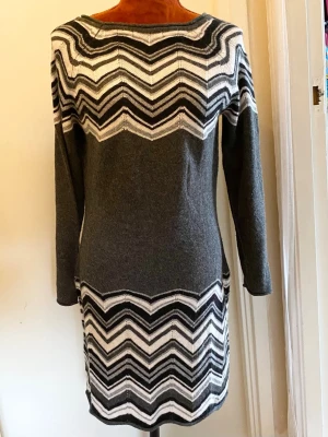 Grå stickad klänning med zigzagmönster M - Klänningen har ett iögonfallande sicksackmönster i svart, vitt och grått som löper över bysten och nederkanten. Resterande del av klänningen är i en enfärgad mörkgrå nyans. Klänningen har långa ärmar och en rundad halsringning. Längd: 87 cm Bystvidd: 47 cm 45% viskos, 20% polyamid, 20% akryl, 10% ull, 5% angora  Inga bilder när den sitter på mig! Katter finns i hemmet!