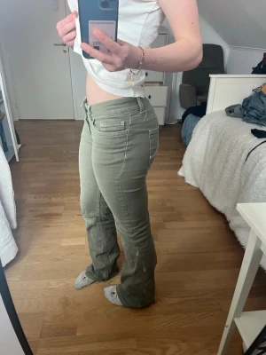 Gröna bootcut jeans med fickor - Snygga gröna bootcut jeans med vita sömmar och klassiska fem fickor. Jeansen har låg midja och är tillverkade i ett stretchigt material som sitter tajt över höfterna och låren. Perfekta för en trendig och avslappnad look.