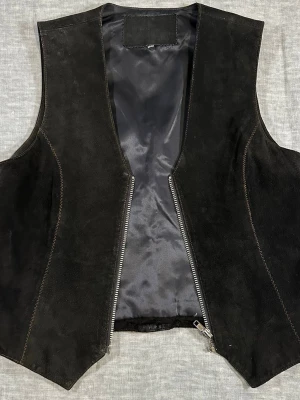 Vintage 90’s Suede Leather Vest Black Western Zip Waistcoat - Authentic 90s black suede vest with sharp western cut + zip front. Minimal cowboy energy, no fringe — just clean lines and fitted silhouette. Perfect layered over baby tee, thermal or slip dress. Real suede with structure, not flimsy.  Size 38/40 (fits M) S2S 36.5 cm P2P 47 cm Waist 46 cm Length 51 cm  Good vintage condition. Normal suede variation. 