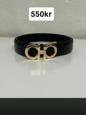 Svart skärp från Salvatore Ferragamo - Snyggt svart skärp från Salvatore Ferragamo med ikoniskt guldigt spänne. Bältet är gjort i slätt skinn och har en elegant, stilren design som passar till många olika outfits.