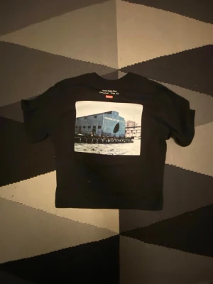 Supreme svart t-shirt  - Svart t-shirt från Supreme i 100% bomull med ett stort grafiskt tryck på bröstet som föreställer en byggnad vid vatten. Klassisk passform och Supreme-logga i nacken. Köptdes för 699 på second place använd en gång ser väldigt cropped ut i bilden fast den sitter normalt