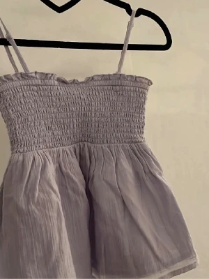 Ljuslila linnetopp - Supersöt ljuslila top från Gina Young med smockad topp och volang längst ner. Man kan ta av banden och använda tröjan som en kjol också! Storleken är 146/152 ungefär som en XXS.