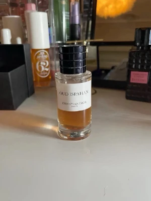 Oud Ispahan parfym från Dior - Lyxig parfym från Christian Dior, Oud Ispahan. Flaskan är cylindrisk i genomskinligt glas med svart räfflad kork och vit etikett. Doften är känd för sina orientaliska och träiga noter, perfekt för dig som gillar exklusiva och djupa parfymer.